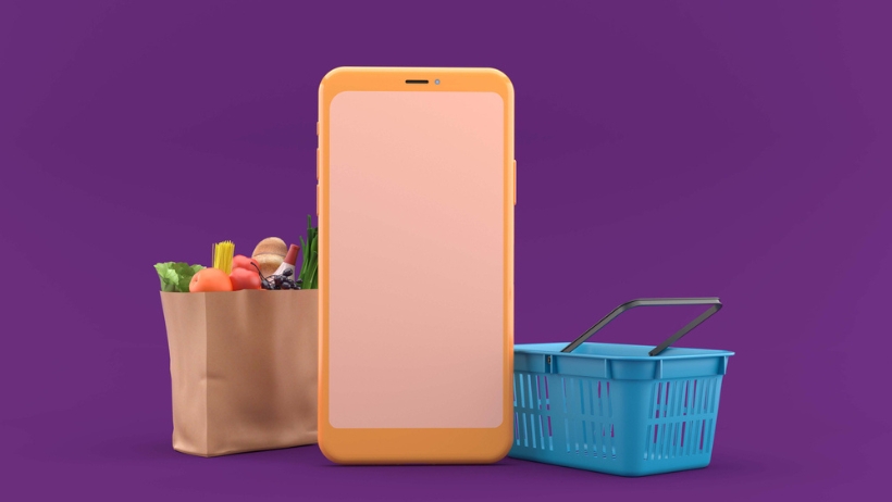 Ein Mobiltelefon mit veganen Lebensmitteln und einer Einkaufstasche auf lila Hintergrund.